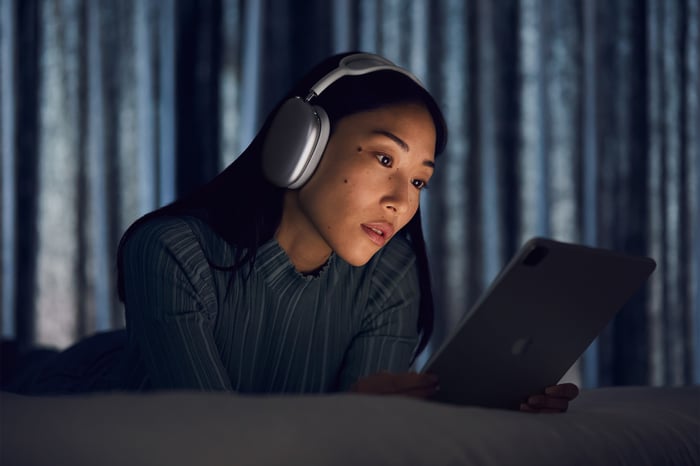 A woman wearing Apple's new AirPods Max headphones while using an iPad.