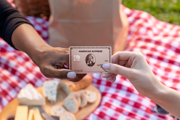 Two people exchanging an AmEx card at a picnic.