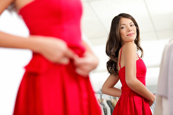 Woman trying on a red dress in a shop as she checks out her reflection.