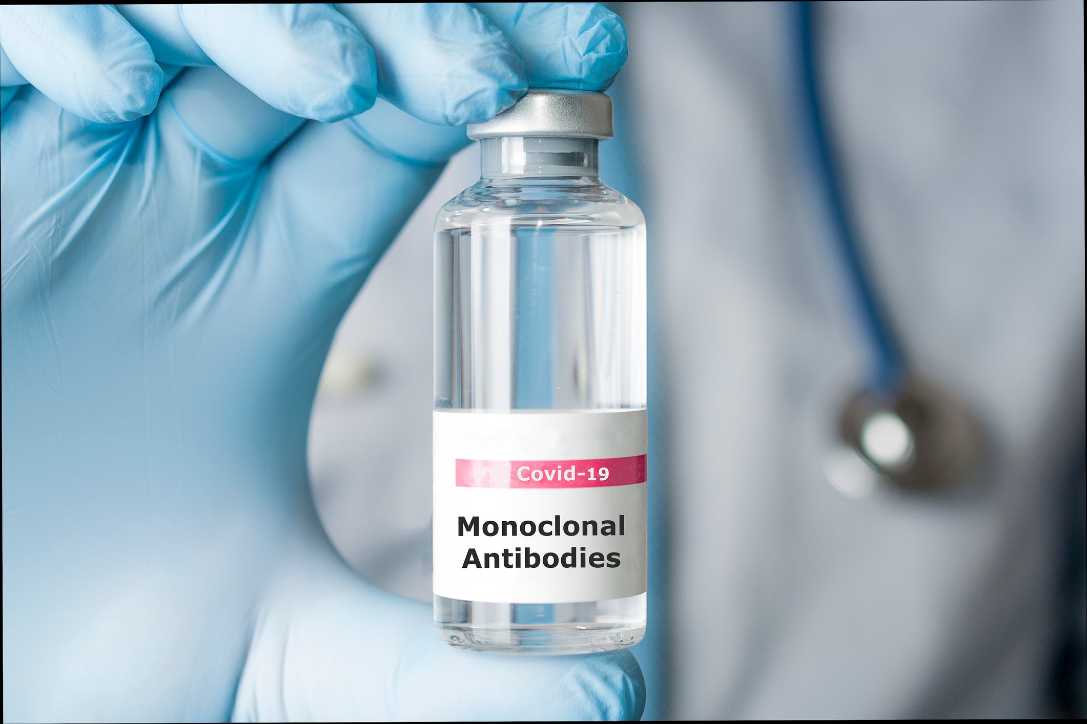 A gloved hand holding a vial of monoclonal antibodies.