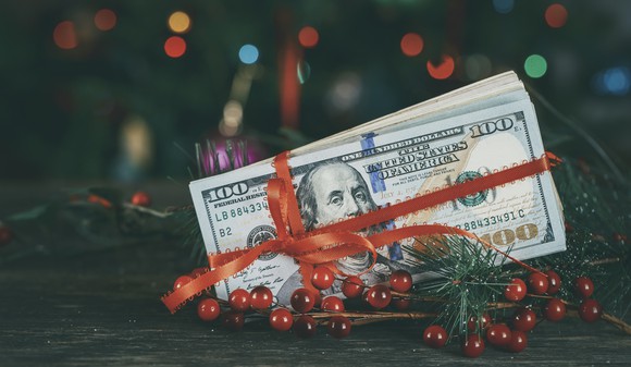 Hundred dollar bills wrapped in red ribbon sitting among Christmas decorations