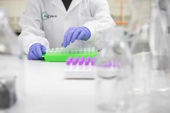 Person wearing purple gloves and AbCellera white lab coat working with pipettes.