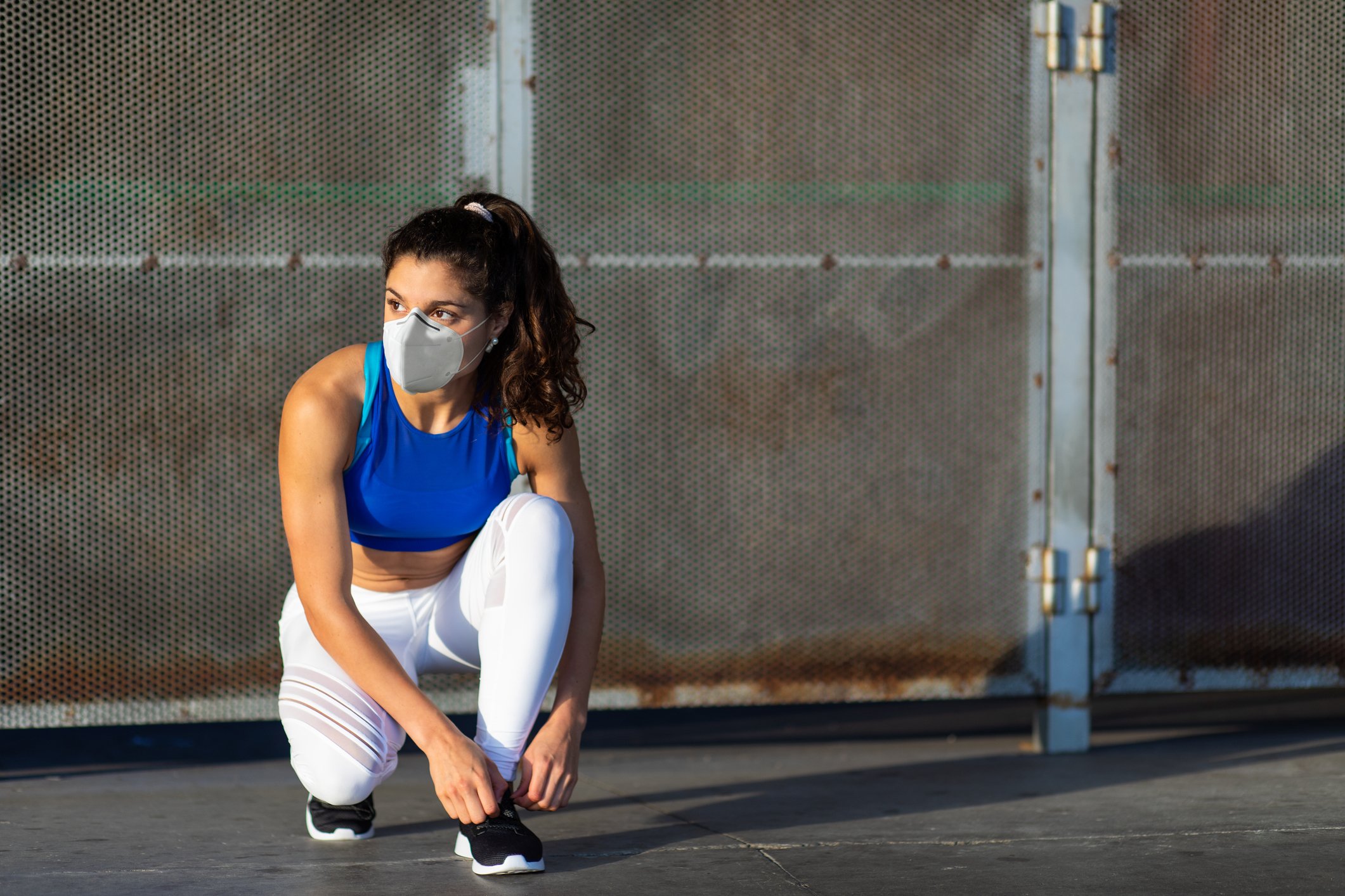 Lady wearing face mask and workout gear bending down to tie her shoelaces