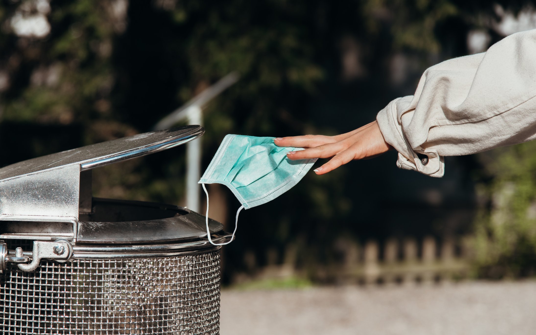 Person throwing a protective mask into a trash can