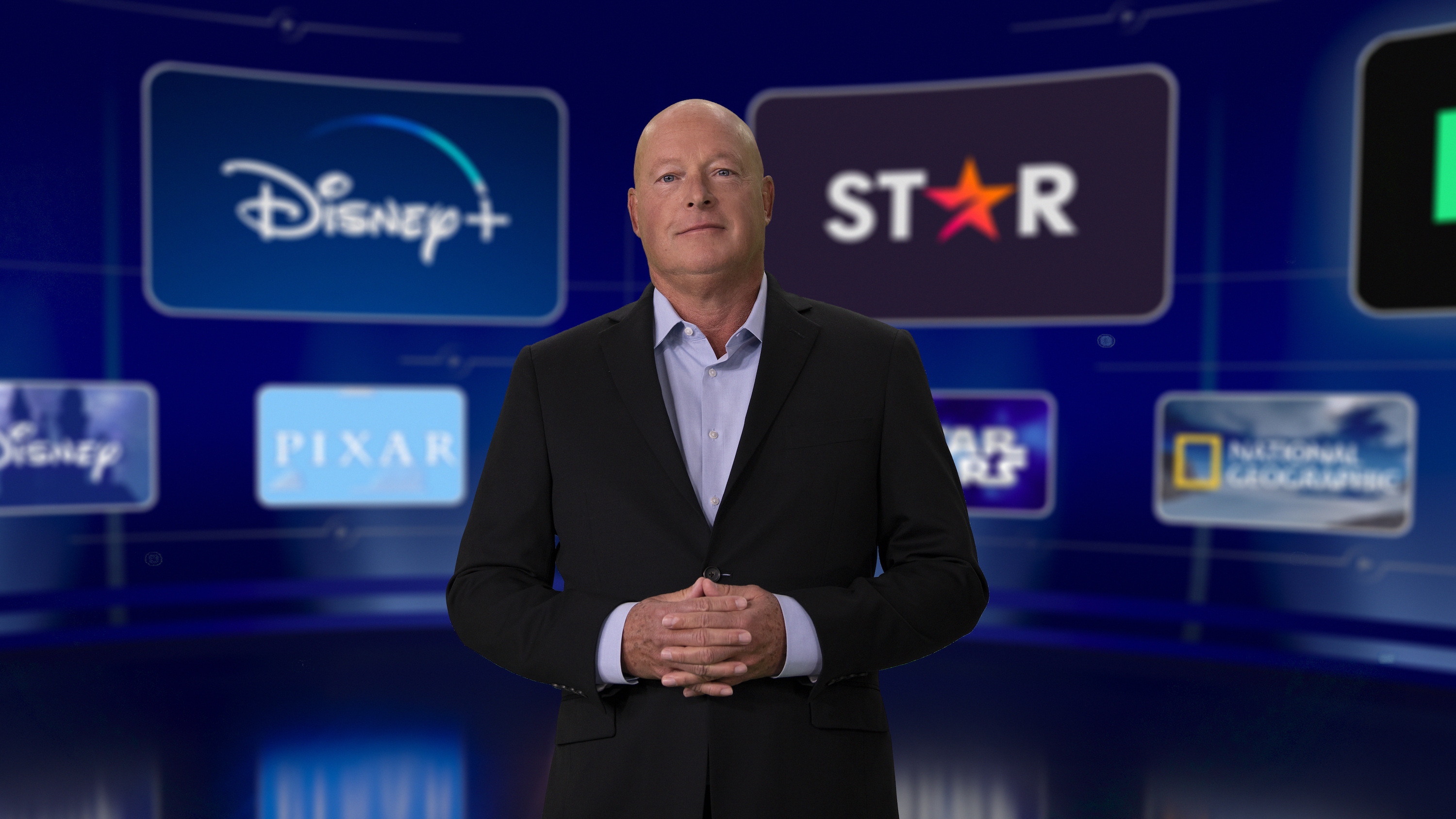 Disney CEO standing in front of a several logos of Disney assets.