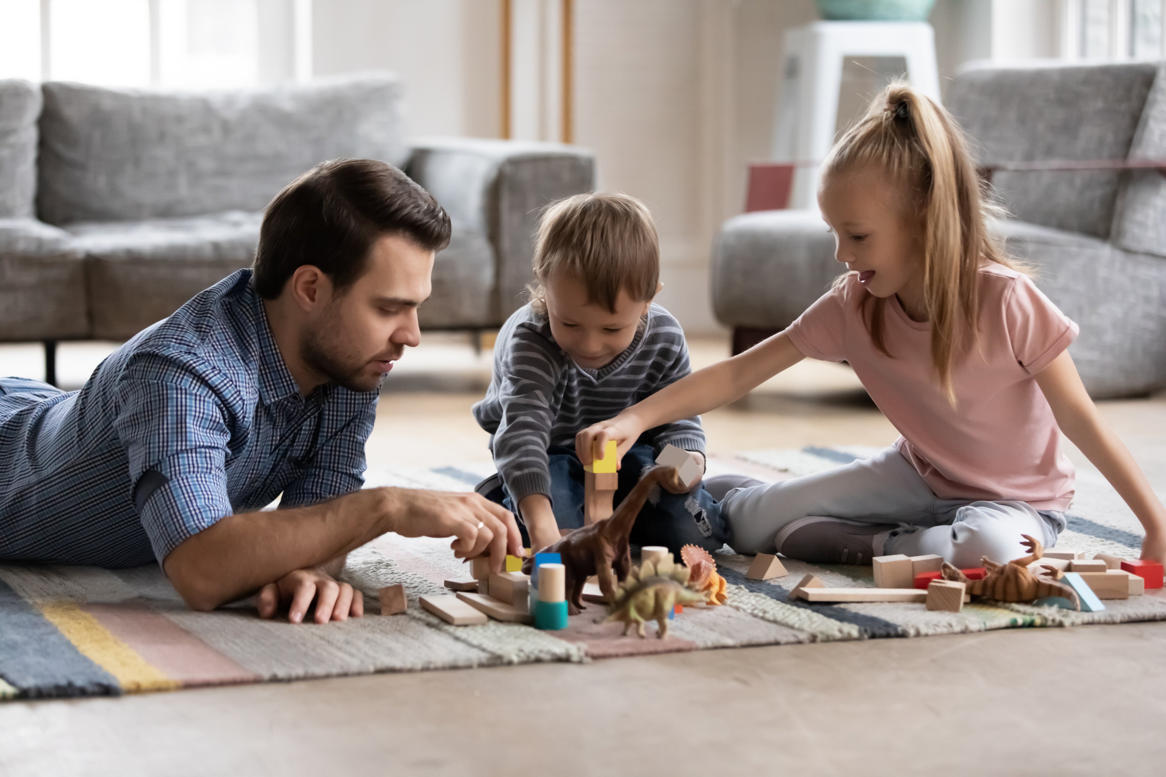 A parent and two children playing with toys on the floor.