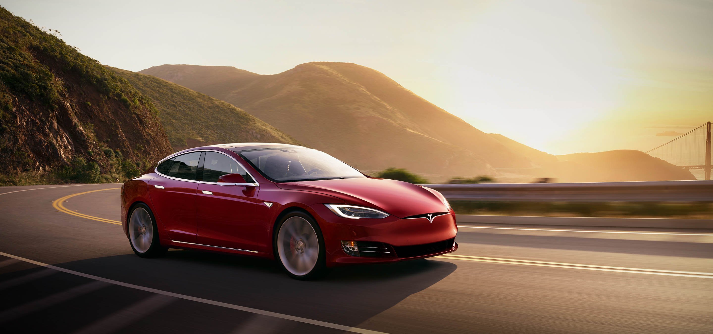 A Tesla Model S driving on a mountain road as the sun rises in the distance. 