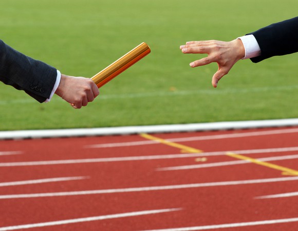Man in suit passing a baton to another man in suit.