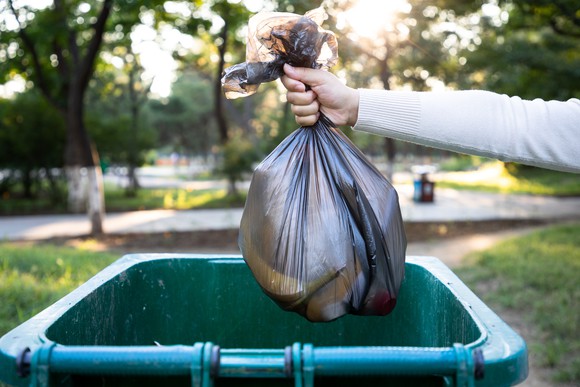 A person throws a bag of trash into a trash bin. 