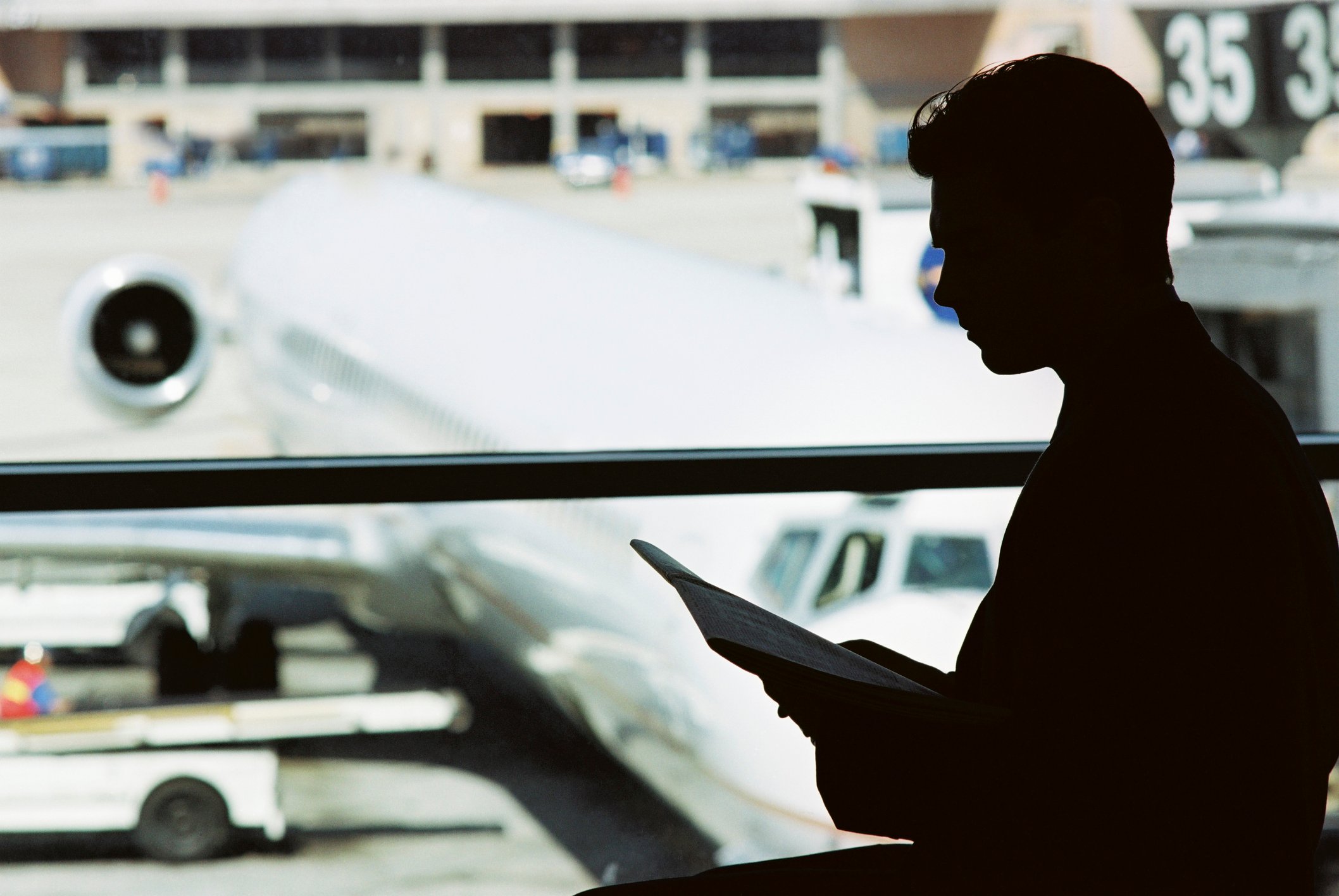 A man is silhouetted in front of an airplane parked on the tarmac.