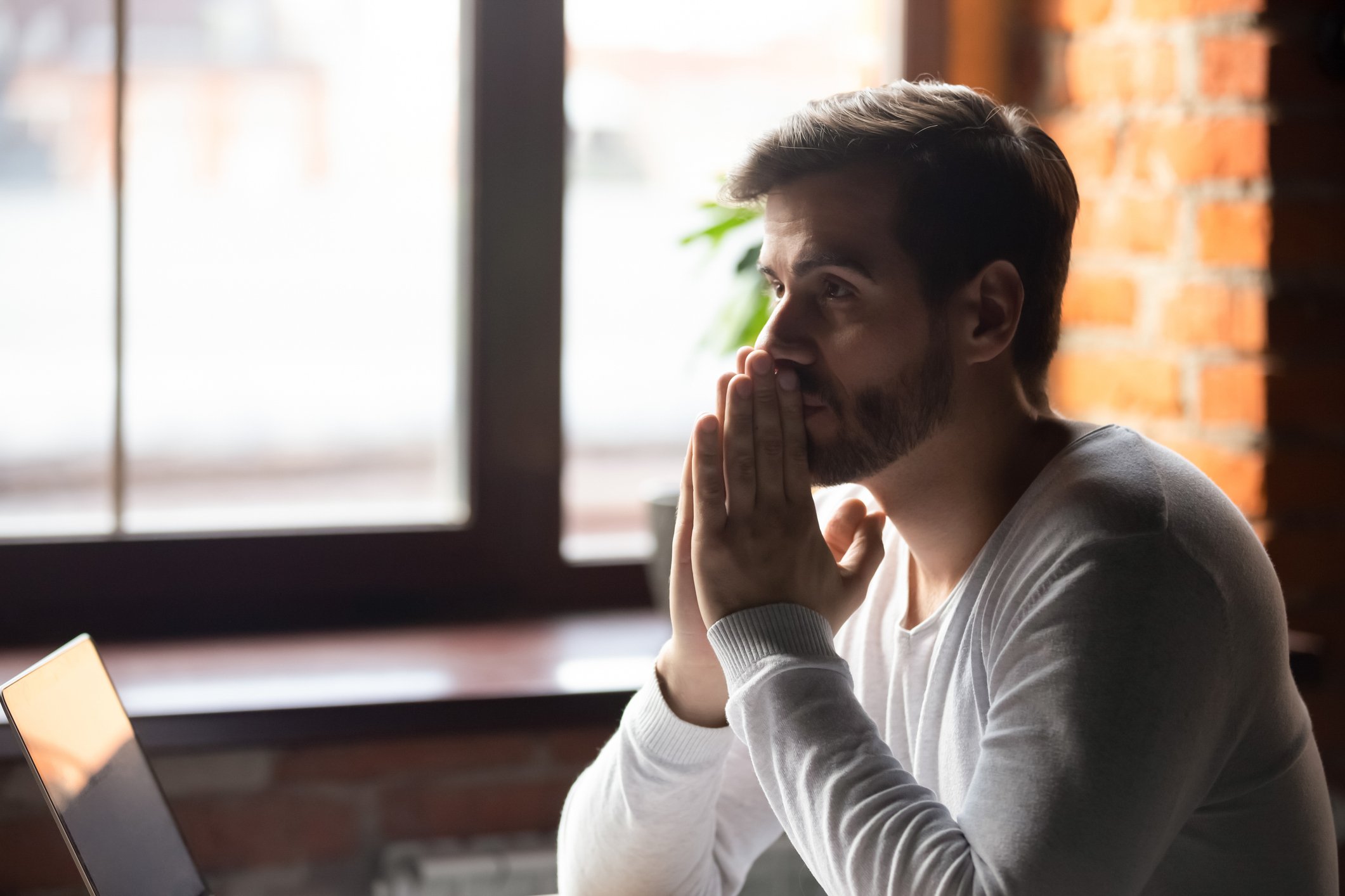 A man with his hands together in front of his face in deep thought, pondering a decision. 