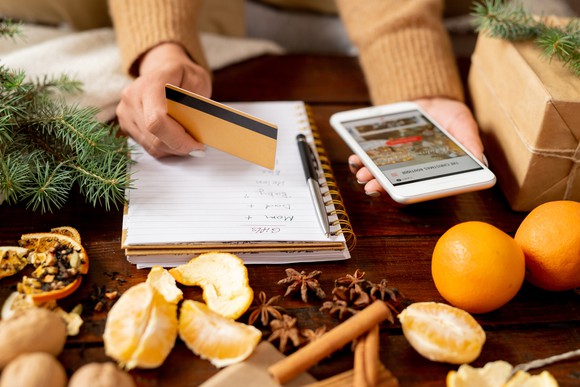 Woman holding credit card and phone on desk decorated with oranges and cinnamon sticks 