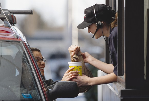 Fast-food restaurant worker handing food to a drive-thru customer.
