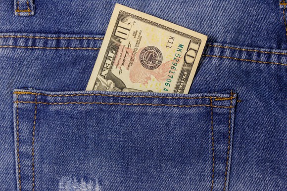 A close up shot of a person wearing blue jeans with a $10 bill sticking up out of the back pocket. 