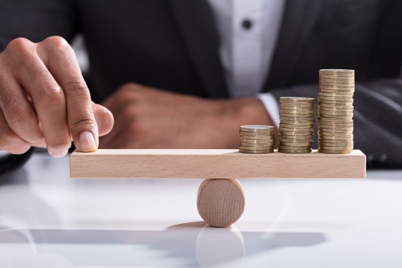 Businessperson balancing stacked coins on wooden seesaw.