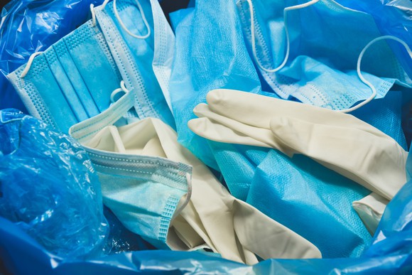 Discarded surgical gloves and face masks sit in a trash bag.