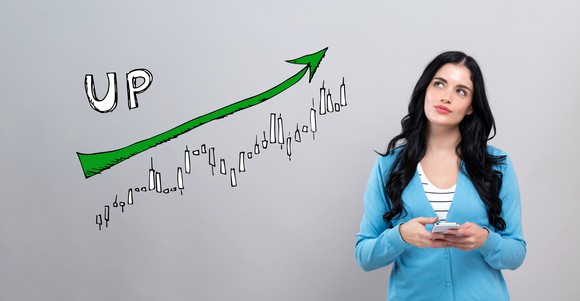 Share prices going up, woman with smartphone looking at the upward stock trend.