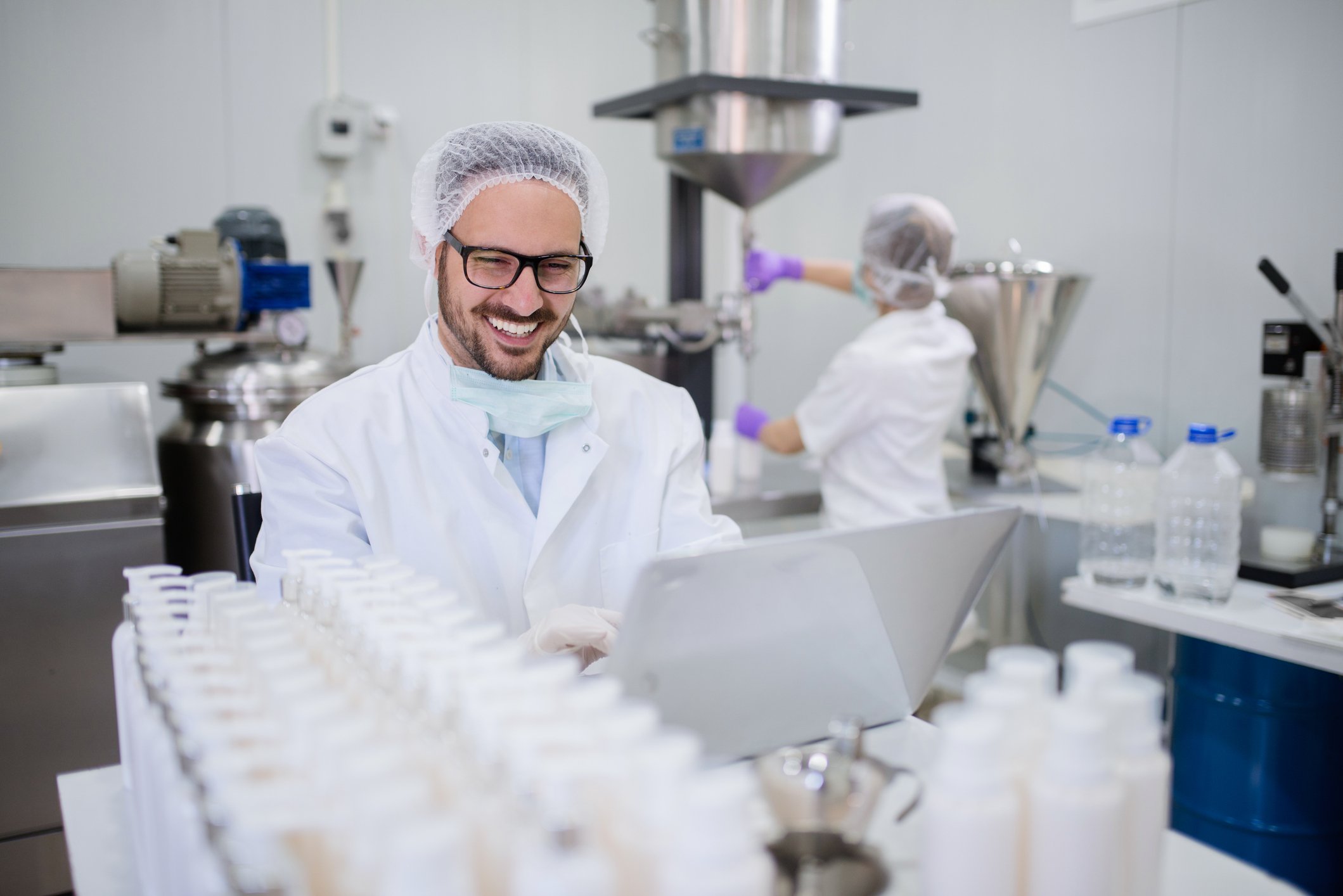 A researcher smiling at a laptop in a pharmaceutical manufacturing facility.