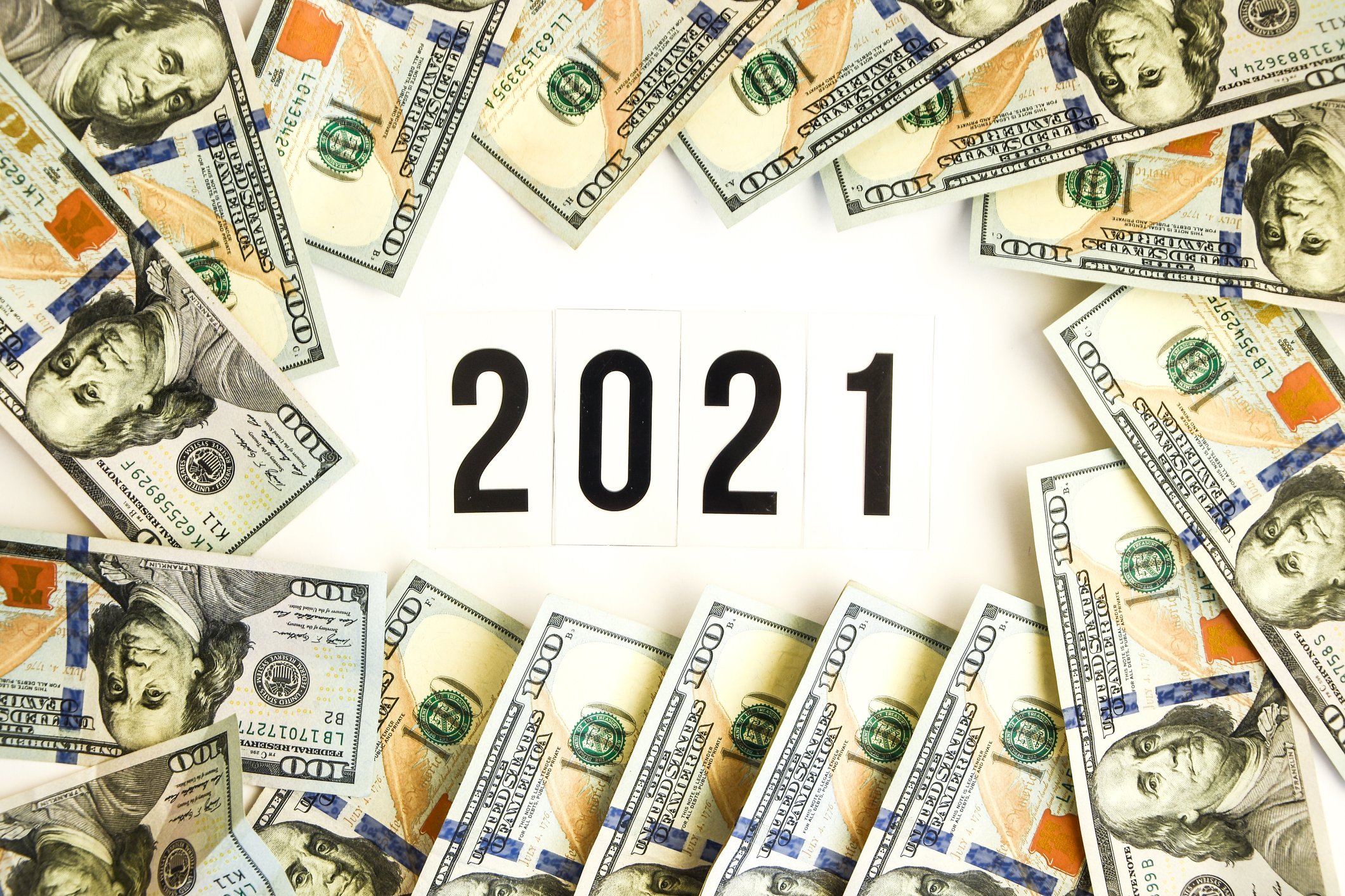 The number 2021 with piles of hundred dollar bills surrounding it.