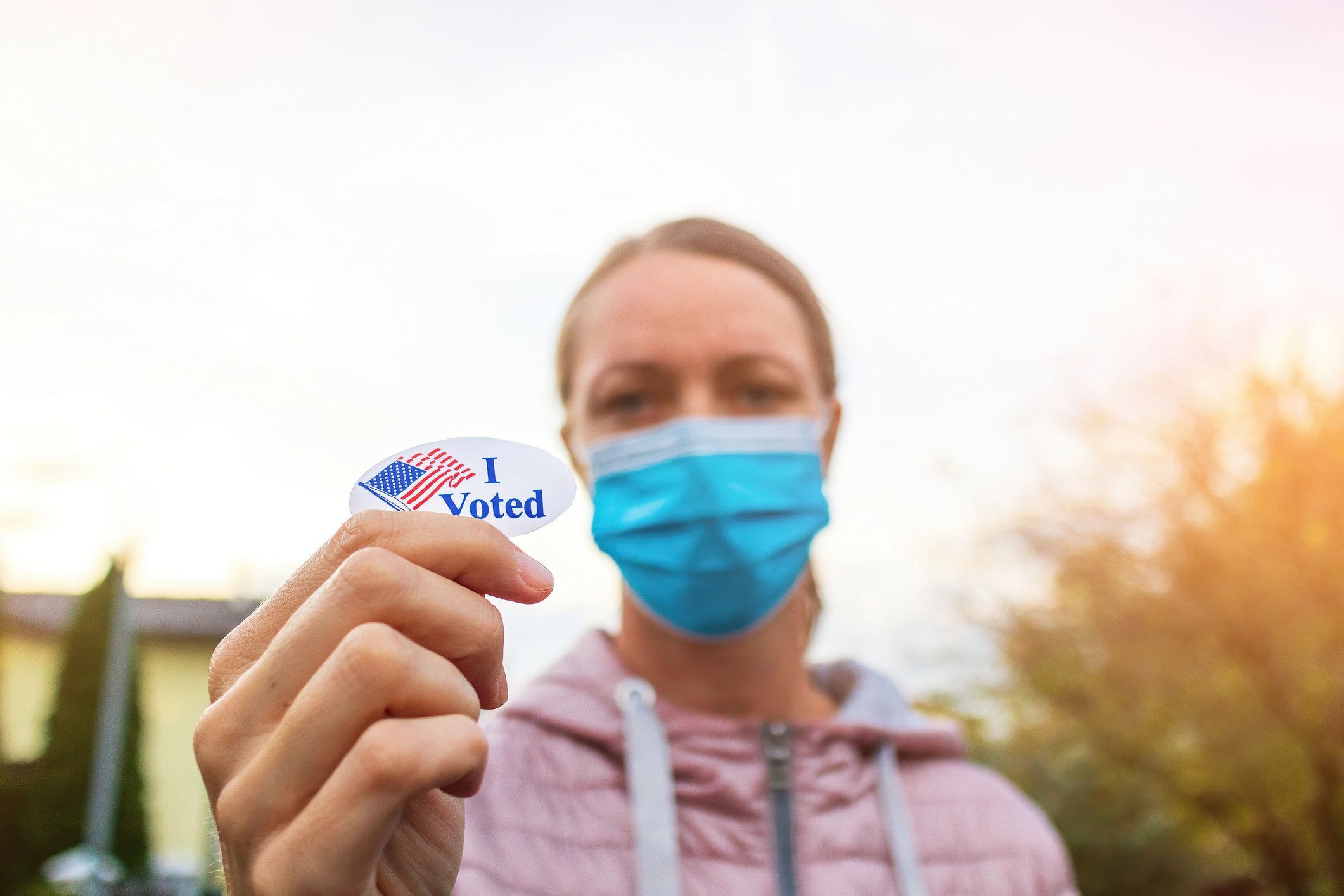 Masked woman holding I Voted sticker.