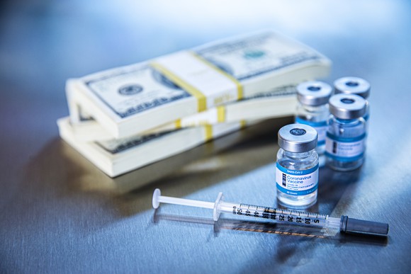 Syringe and four vaccine vials next to stacks of cash