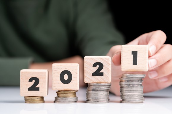 Man putting a wood block with a 1 printed on it on top of a stack of coins to form "2021" on four ascending stacks of coins