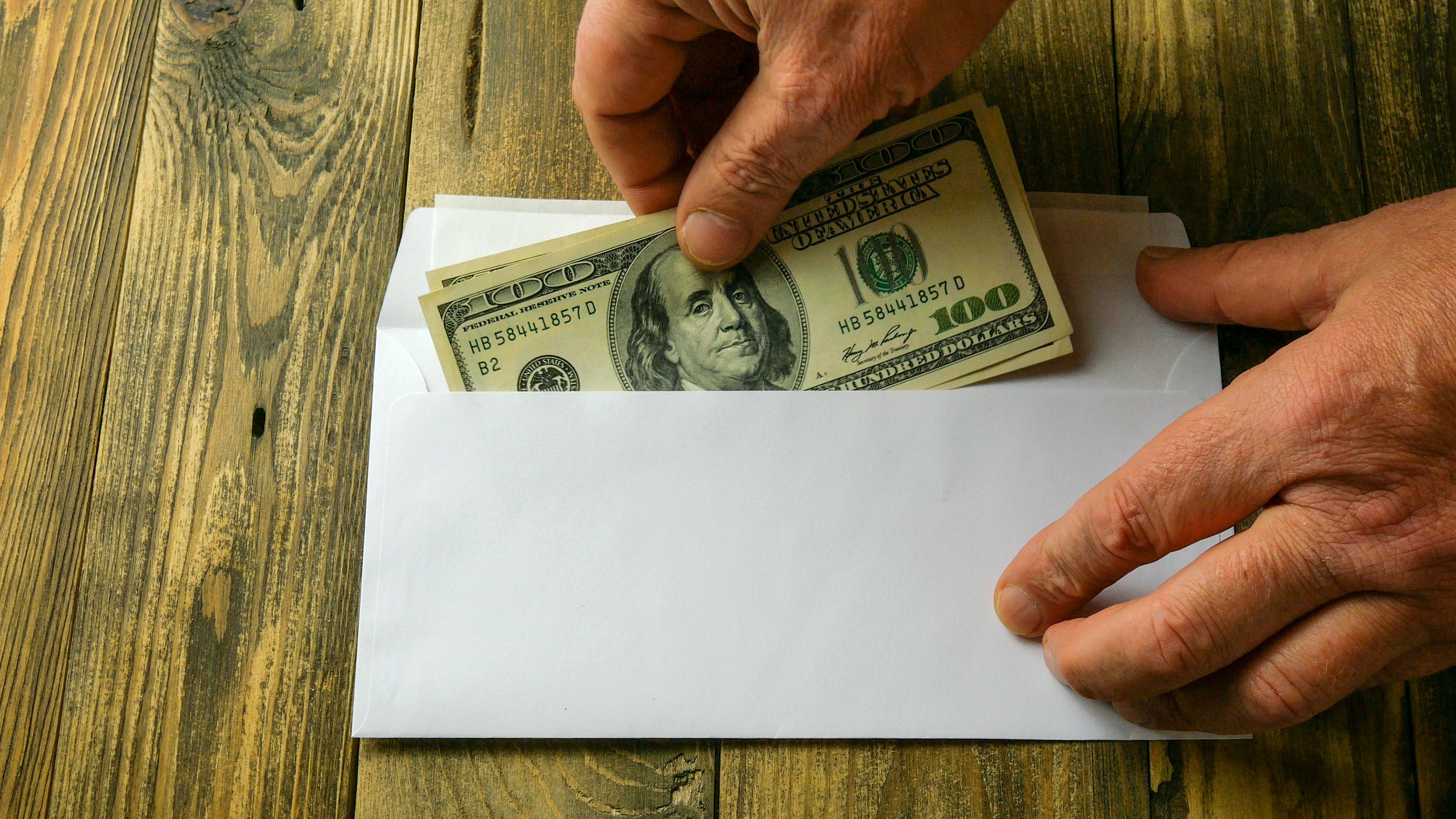 A hand is pulling $100 bills out of an envelope.