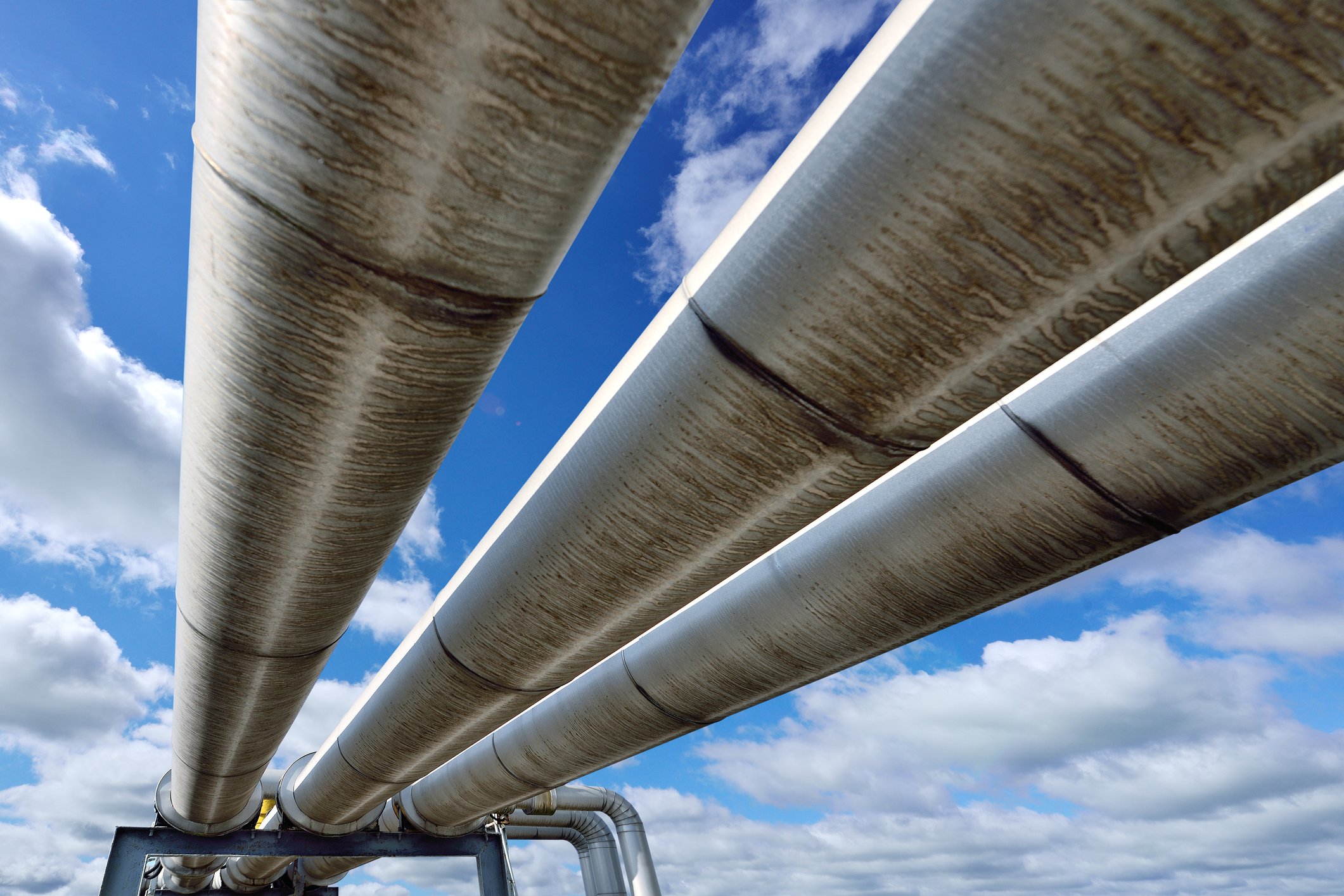 Looking upward at three oil pipelines with the sky in the background