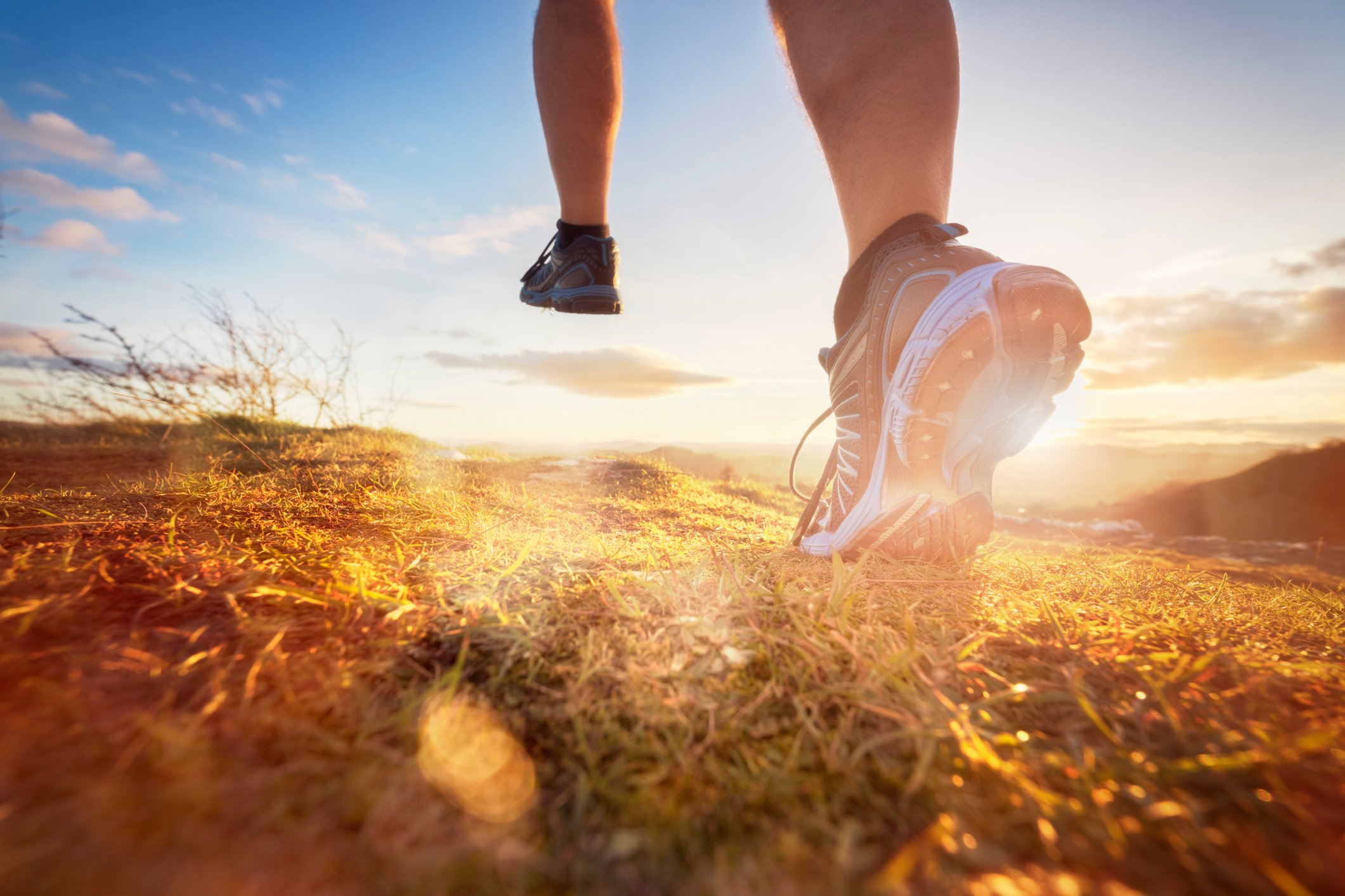 A pair of legs running in athletic shoes against a bright sunrise. 