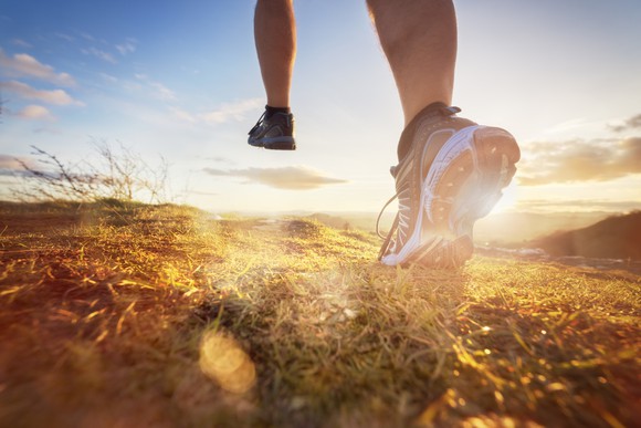 A pair of legs running in athletic shoes against a bright sunrise. 