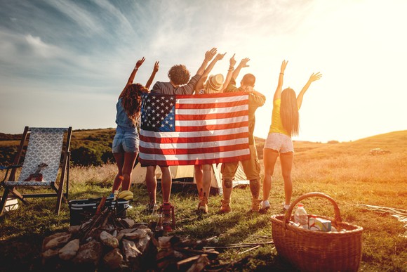 A group of friends outdoors holding an American flag at their backs.