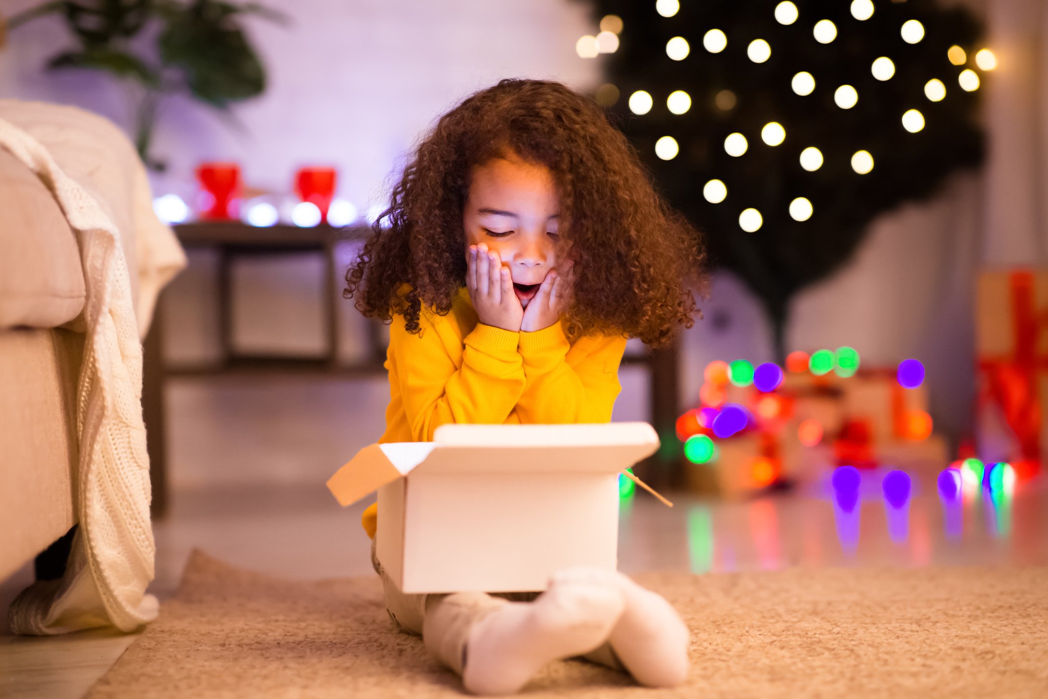 Amazed little girl opening Christmas gift near Christmas tree. 