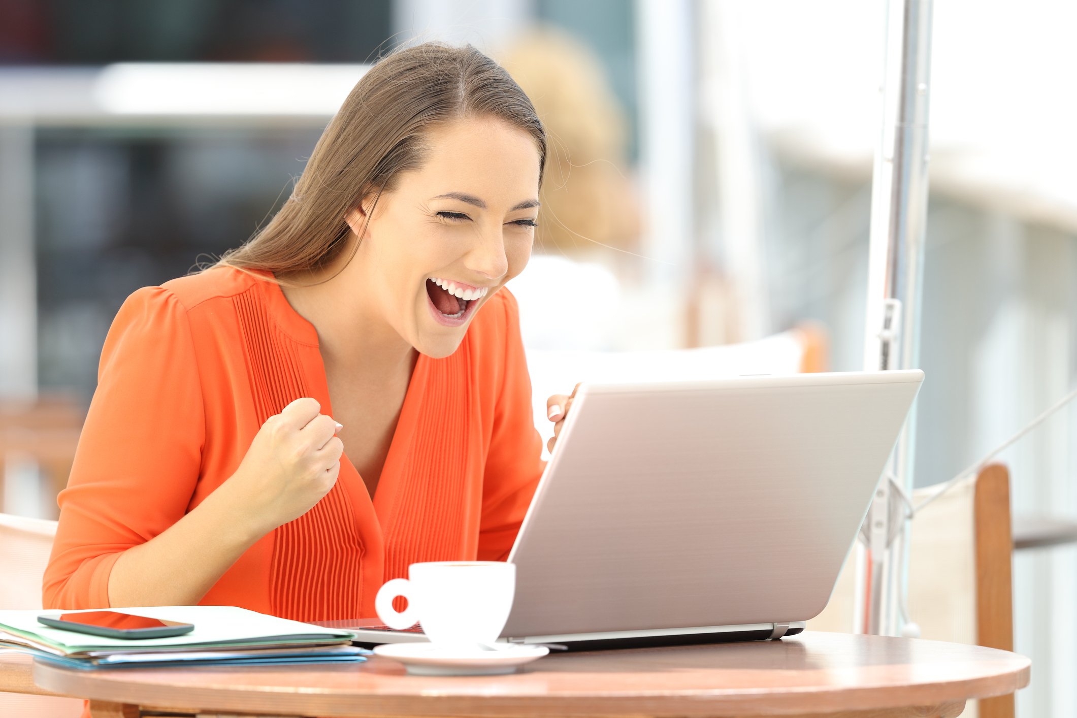 Smiling person using a laptop at an outdoor cafe. 