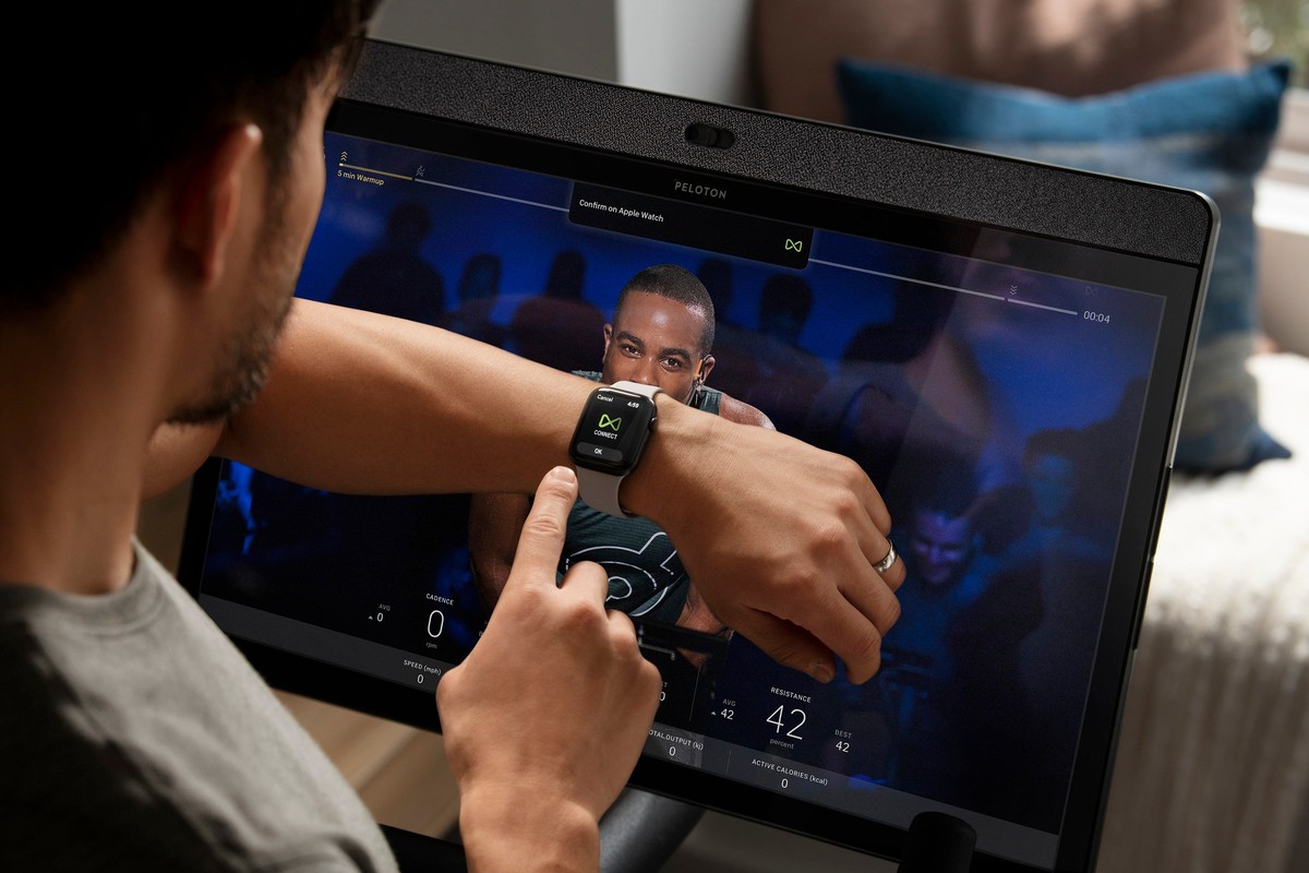 Person on Peloton bike watching screen and using watch.
