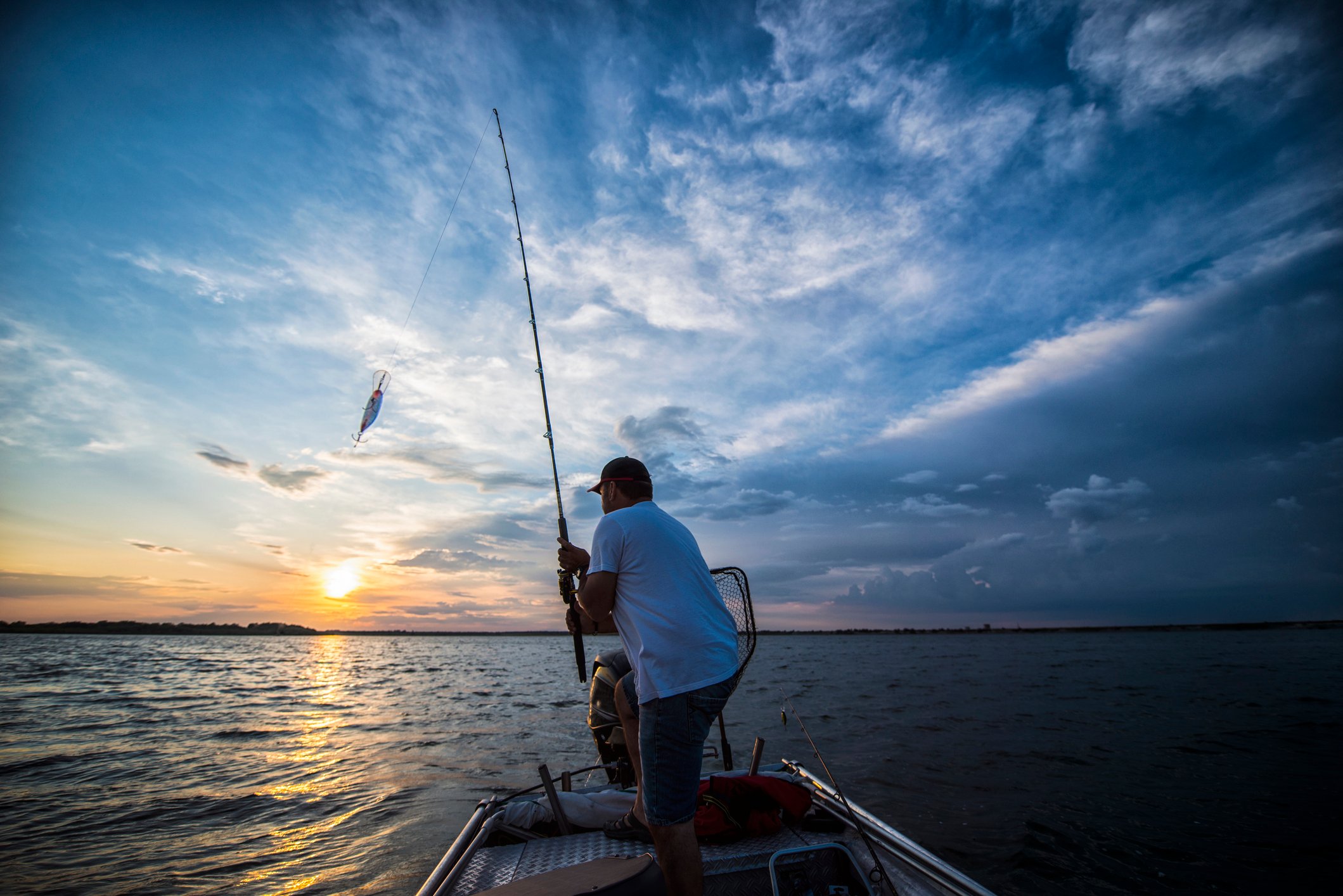 A fisherman on a small boat catching a fish from a lake at sunrise or sunset. 