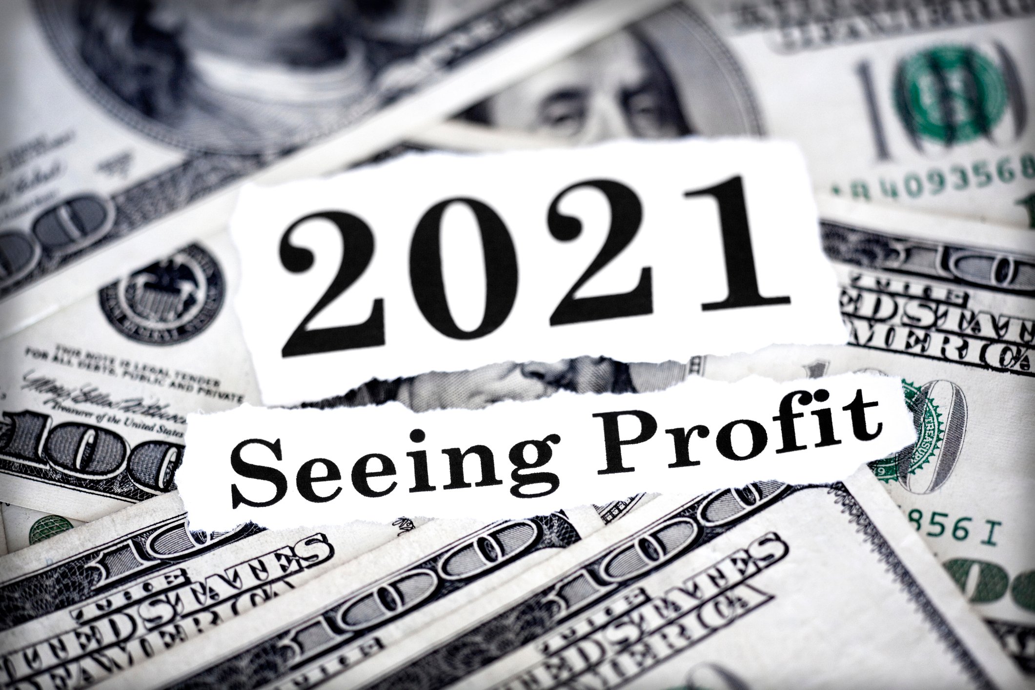 Sign that says "2021, seeing profit" amid a lot of $100 bill. 