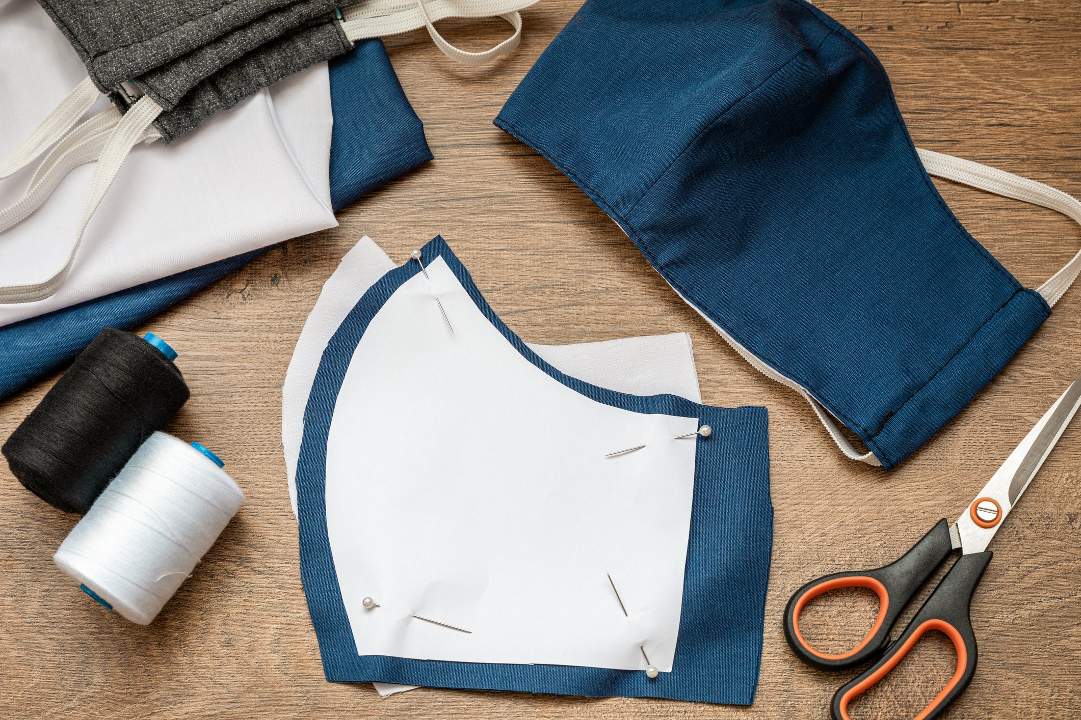 A cloth mask being made with scissors, pins, and thread.