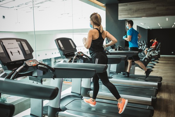 People jogging on gym treadmills while wearing face masks.