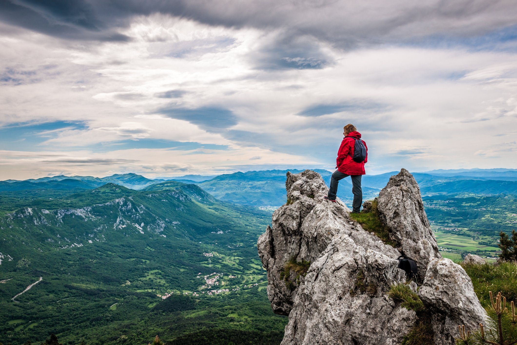 A woman stands on a mountain top and looks out over the landscape. 