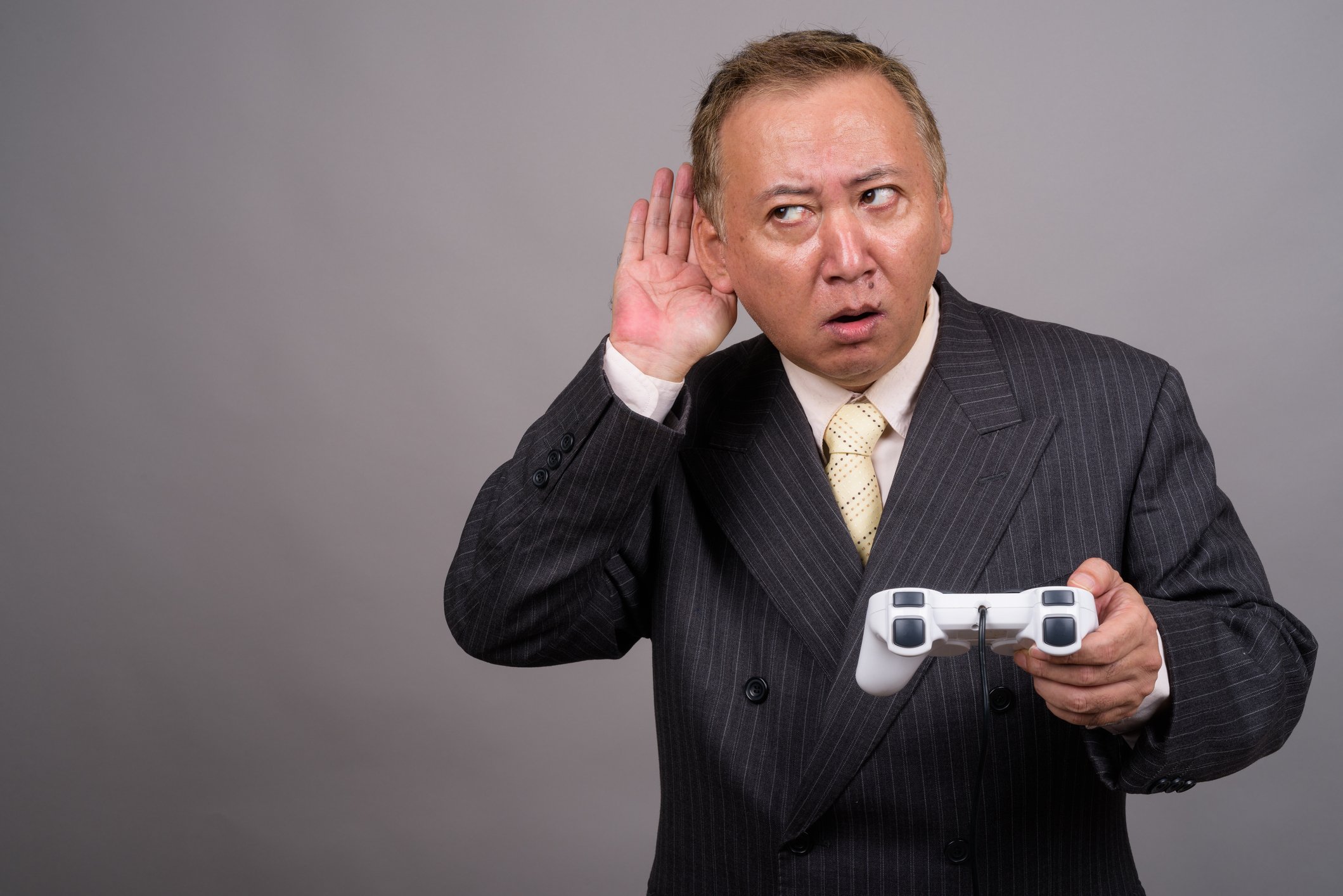 A businessperson holding a video game controller cups his ear and glances sideways.