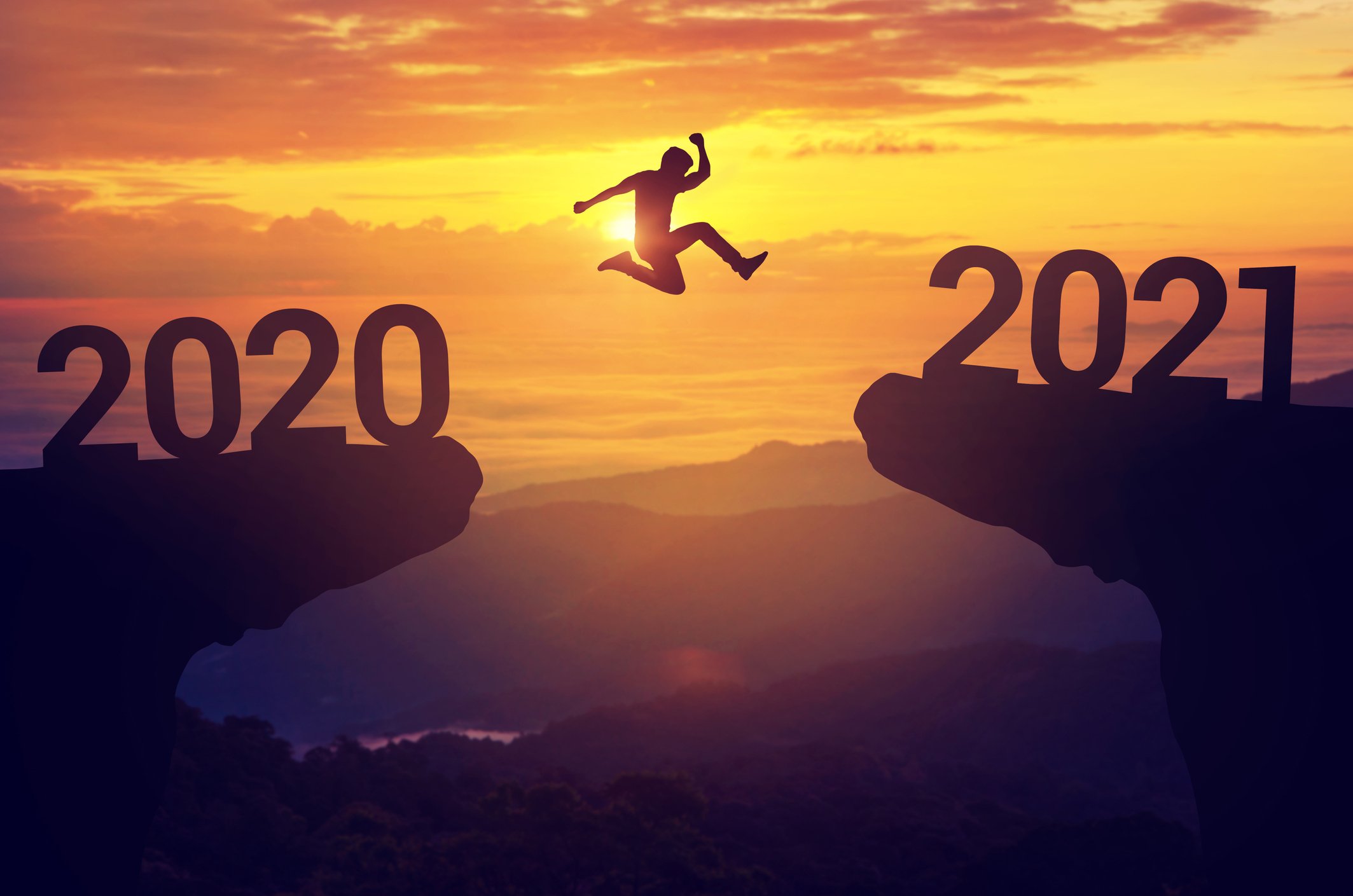 Man jumping across a cavern from 2020 to 2021 as the sun sets.