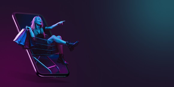 A young woman in a shopping cart emerges from a large phone.