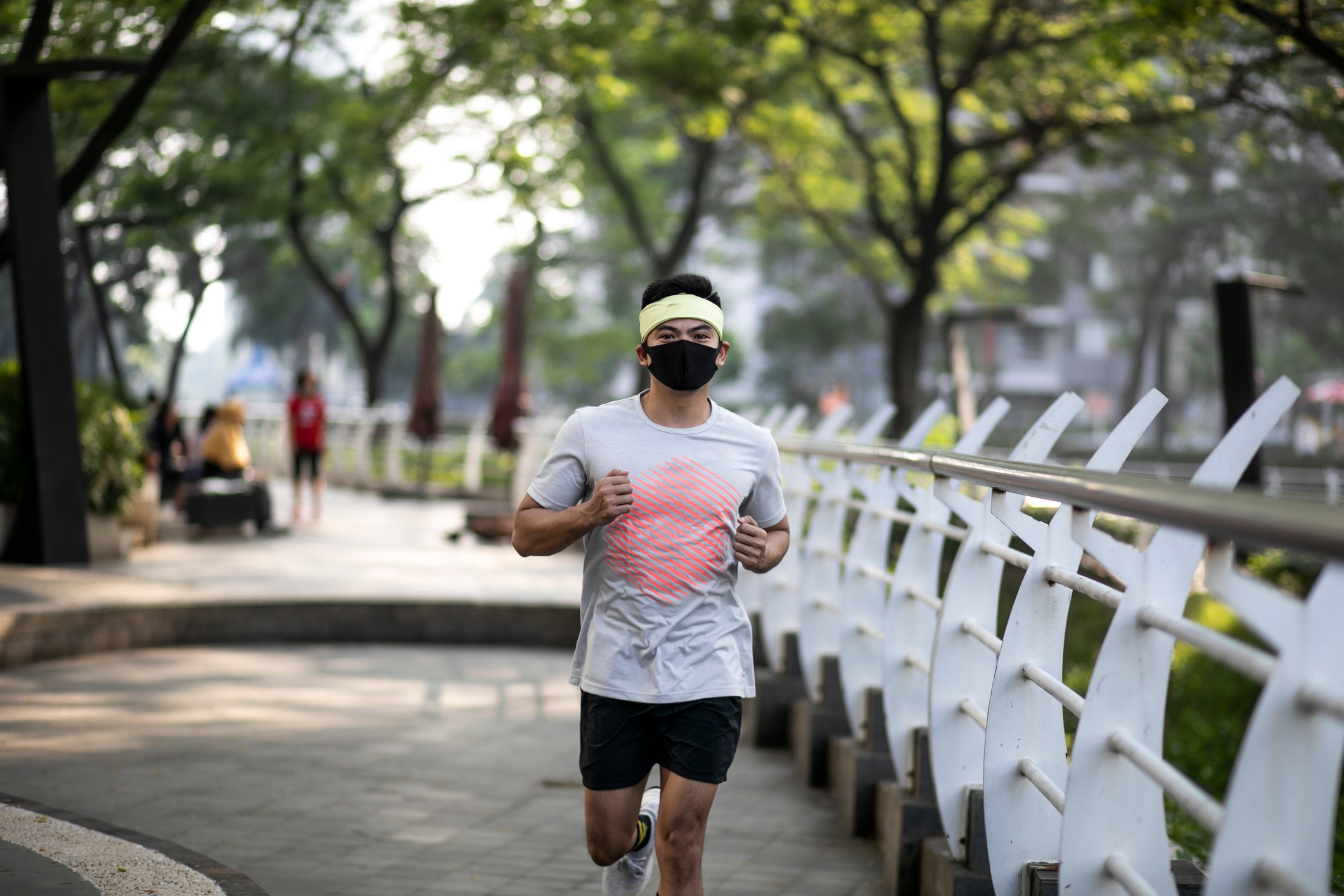 Man in face mask running along a bridge.