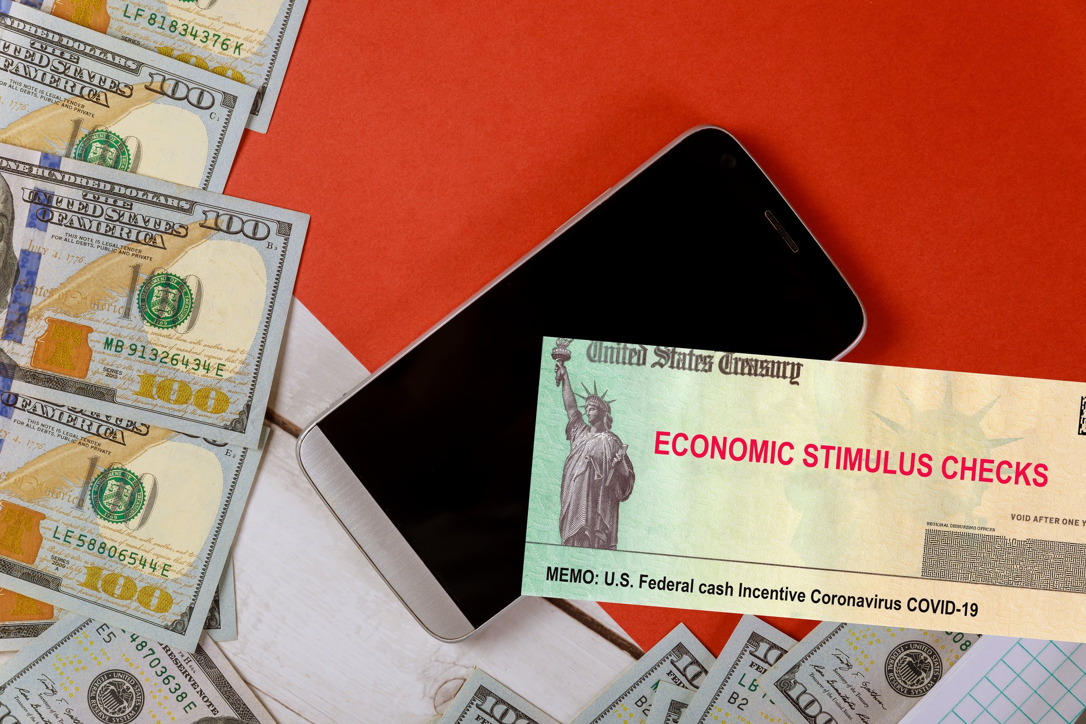 Economic stimulus check next to smartphone and $100 bills