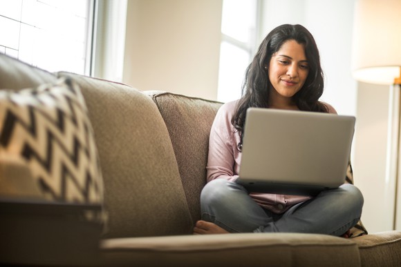 Woman sitting with crossed legs on a sofa looking at a laptop