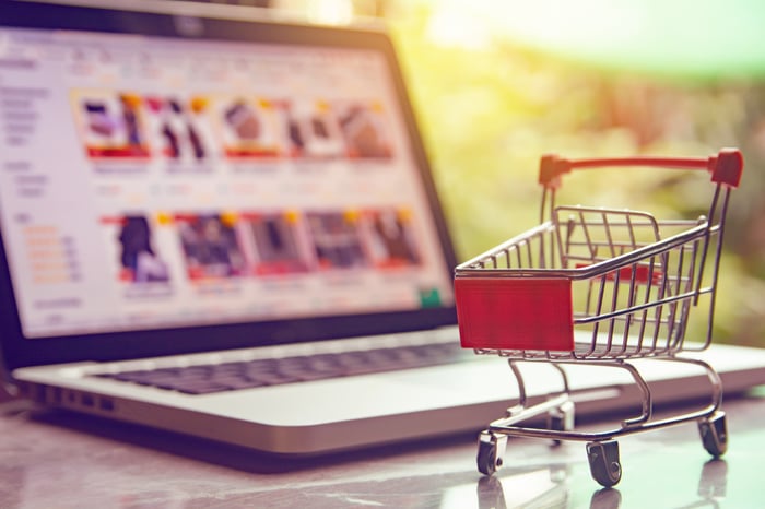 A grocery cart with an e-commerce site running on a laptop in the background.