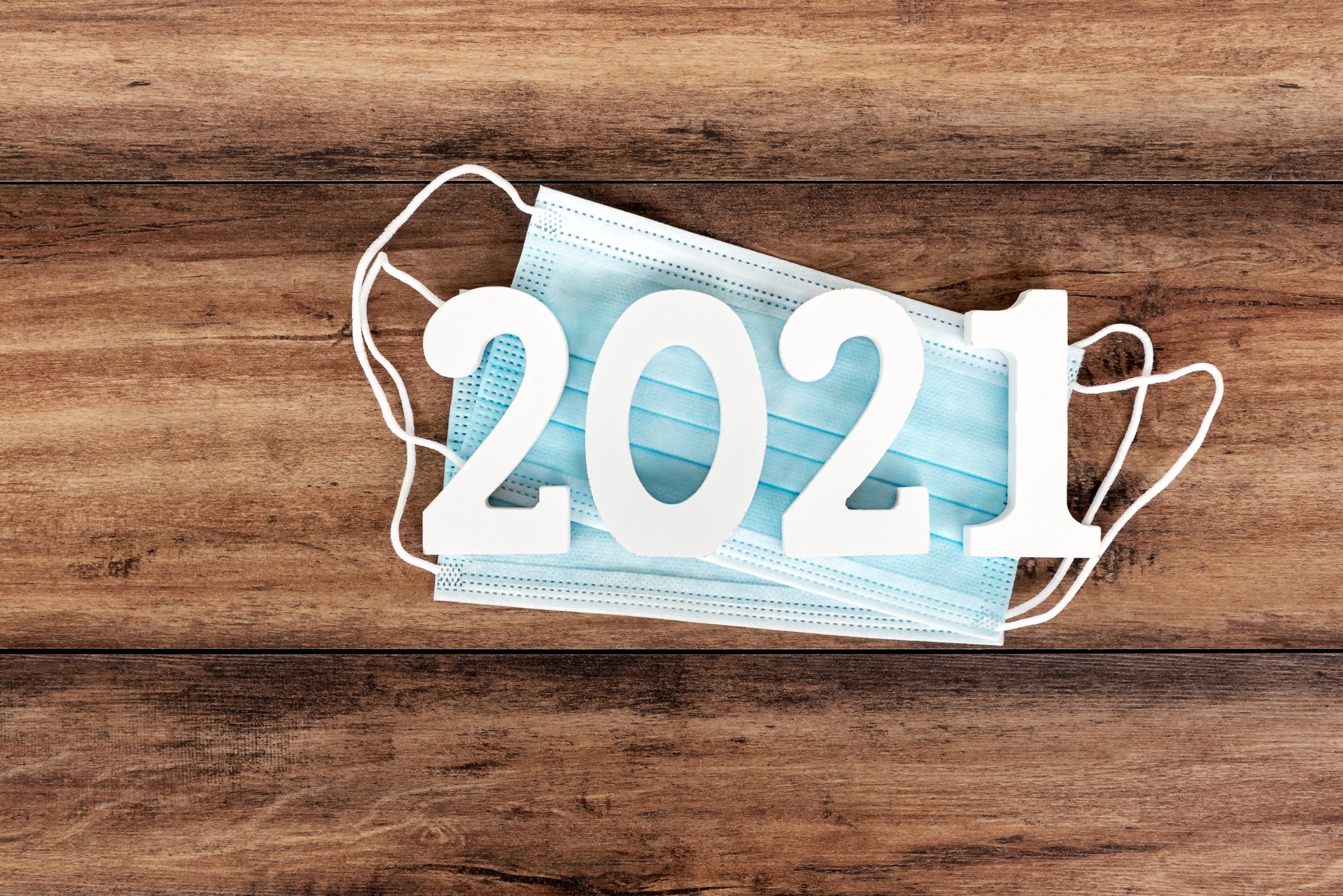 The year 2021 is written over blue face masks set on a wooden surface.