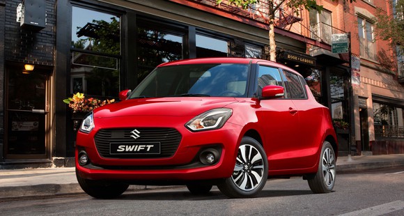 A red Maruti Suzuki Swift, a small two-door hatchback, on a city street. 