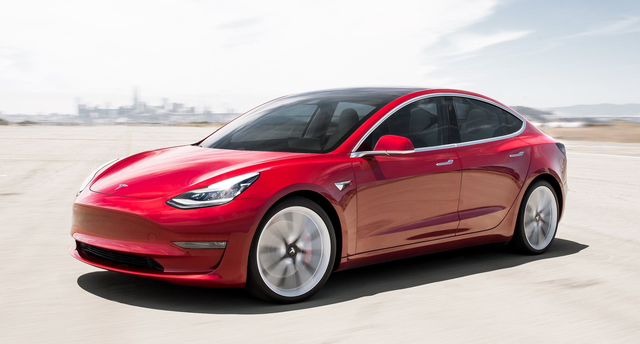 A red Tesla Model 3, a compact electric luxury-performance sedan.