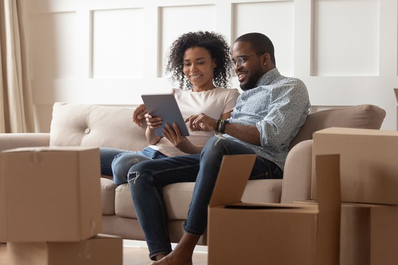 A couple sitting on a couch looking at a tablet, smiling.
